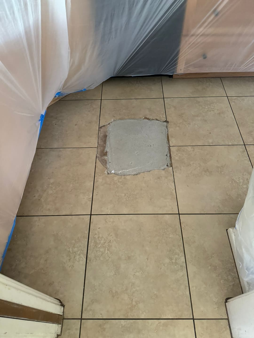 Repair area on tiled floor with fresh concrete patch, surrounded by plastic sheeting.