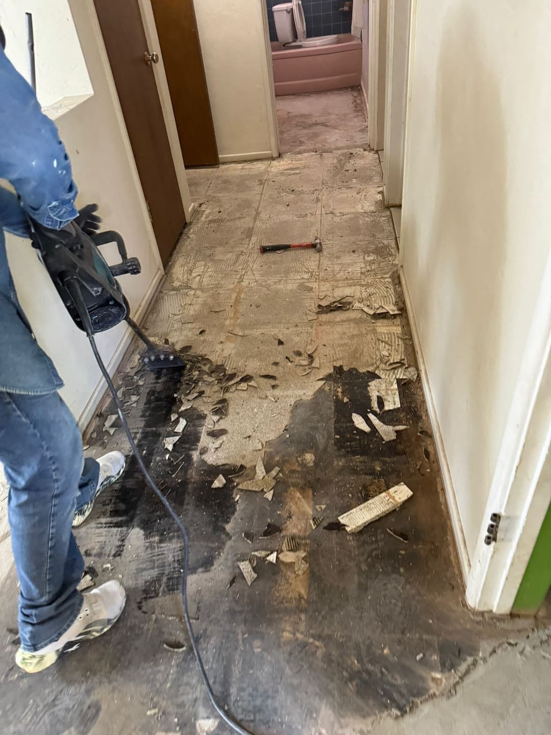 Person using a power tool to remove flooring in a partially renovated hallway.