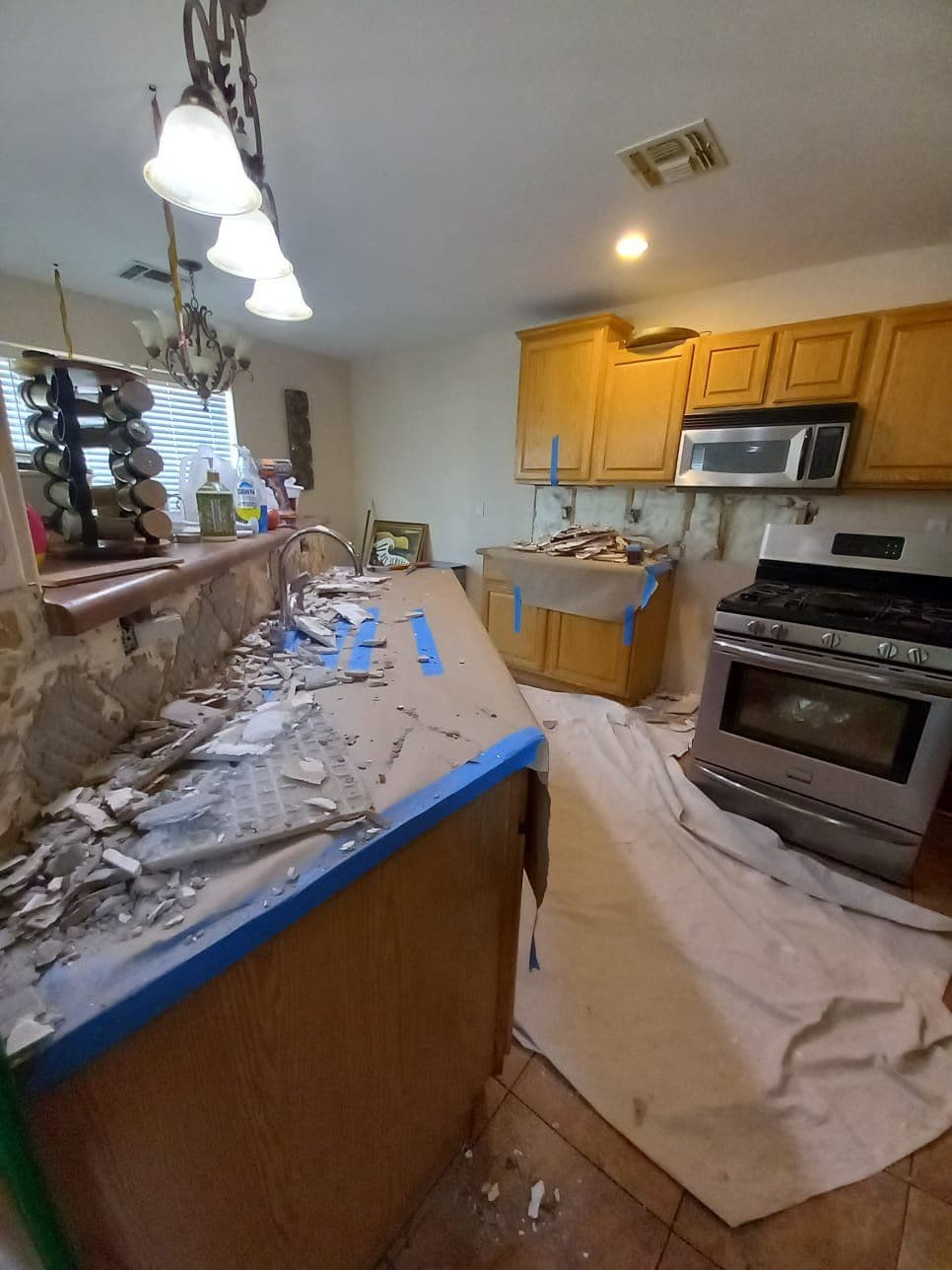 Renovating kitchen with exposed cabinets, debris, and protective cover on the floor.