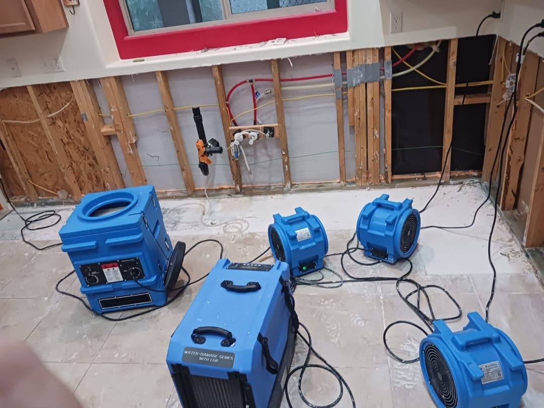Water damage restoration equipment in a kitchen with exposed walls and flooring.