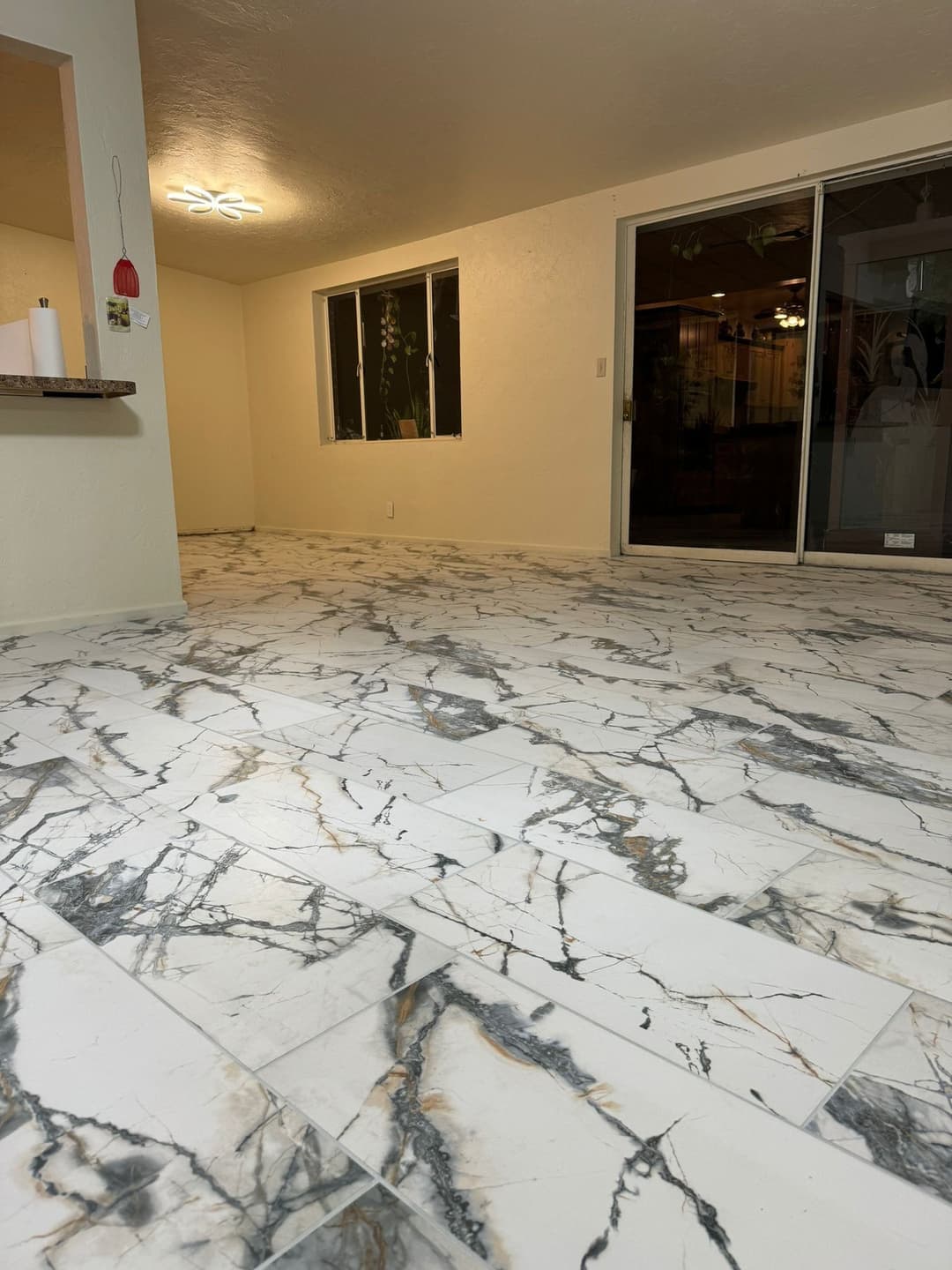 Interior view of a spacious room with marble-patterned tile flooring and large windows.