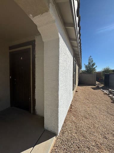Exterior view of a house entrance with door and gravel pathway under a clear blue sky.