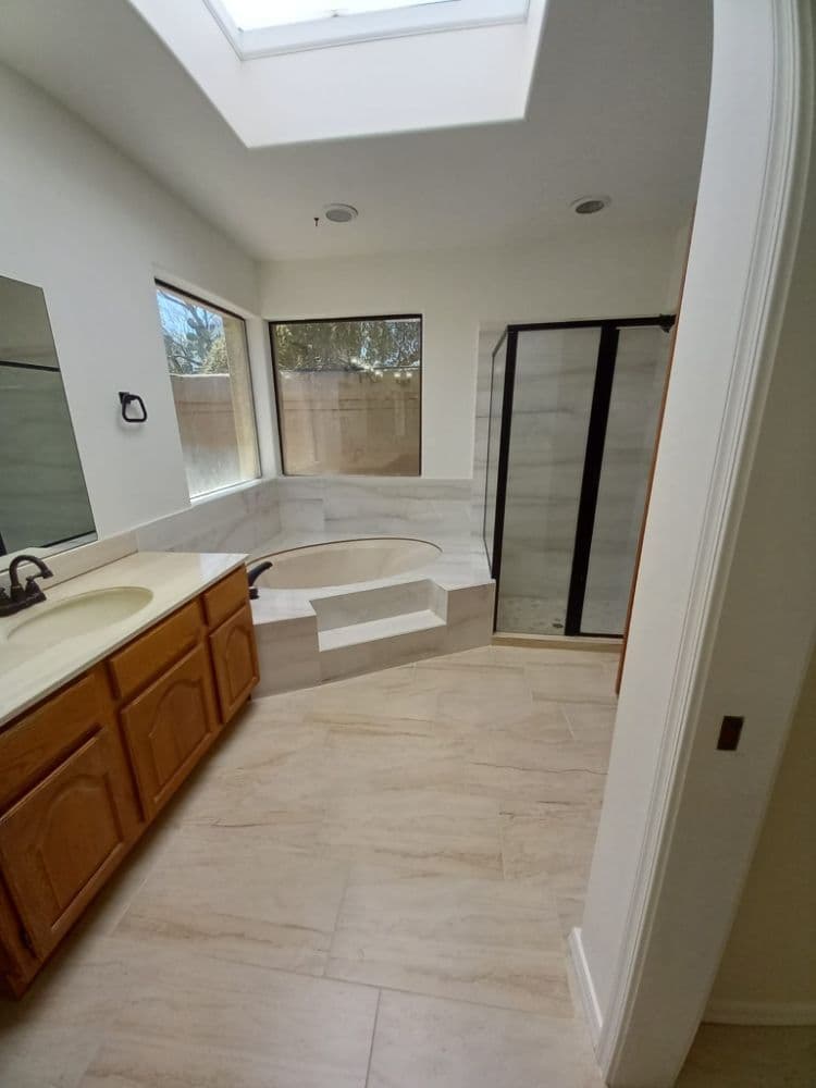 Bright bathroom with skylight, bathtub, and shower. Elegant tile flooring and wooden cabinets.