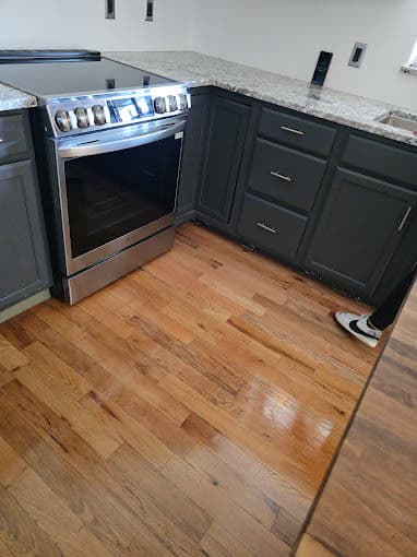 Modern kitchen featuring a stainless steel oven and dark cabinets with hardwood flooring.