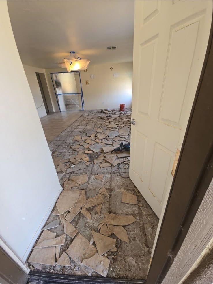 Interior of a room with torn flooring and a partially open door, showcasing renovation progress.