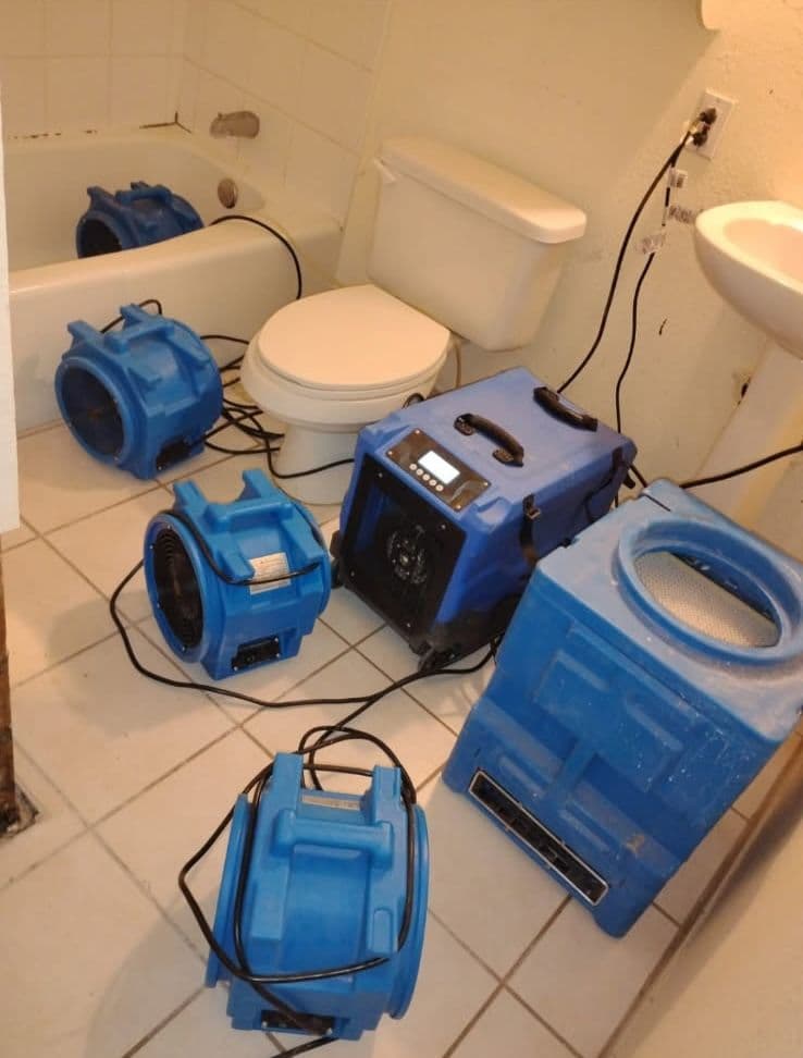 Blue water damage restoration equipment in a residential bathroom with a bathtub and toilet.