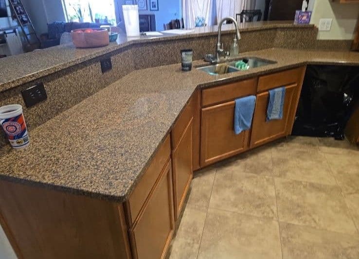Granite kitchen countertop with wooden cabinets, sink, and blue towels hanging.