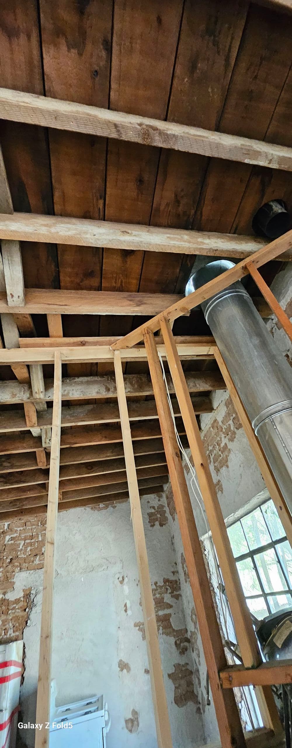 Exposed wooden ceiling beams and framework in a partially renovated room.