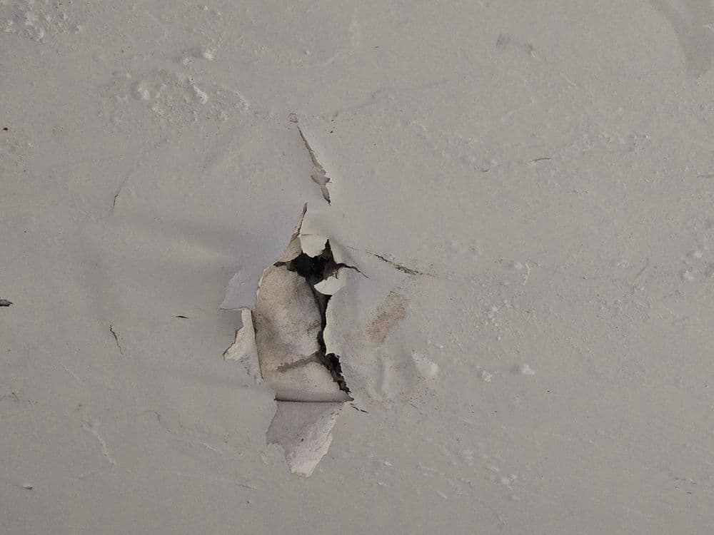 Damage on a wall with peeling paint and a visible hole, indicating wear and tear.